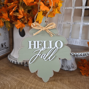 Sign farmhouse Hello Fall en forme de feuille vert sauge avec inscription blanche et nœud en raphia